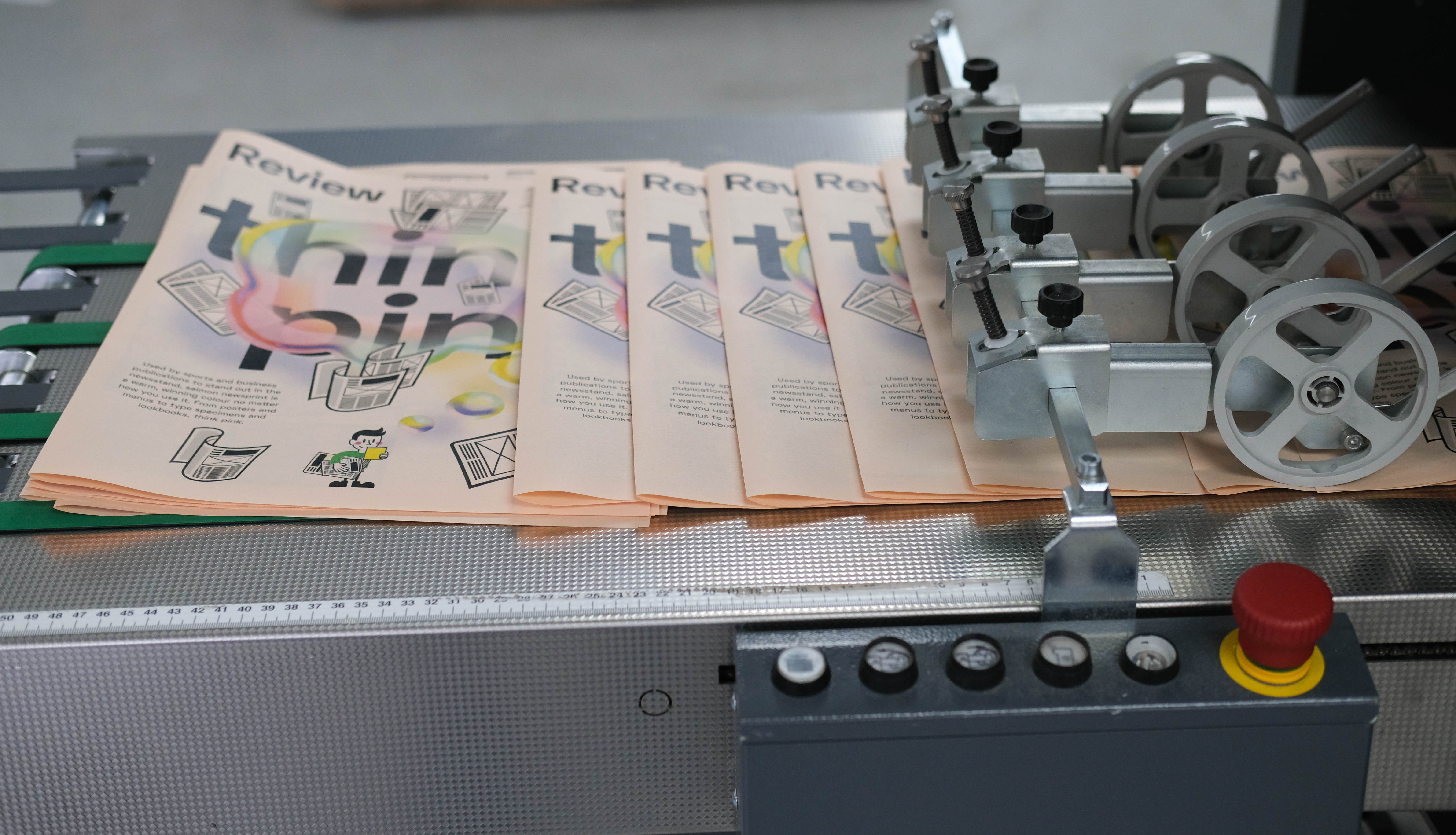 Tabloid newspapers on salmon paper being printed on Newspaper Club’s digital printing press.