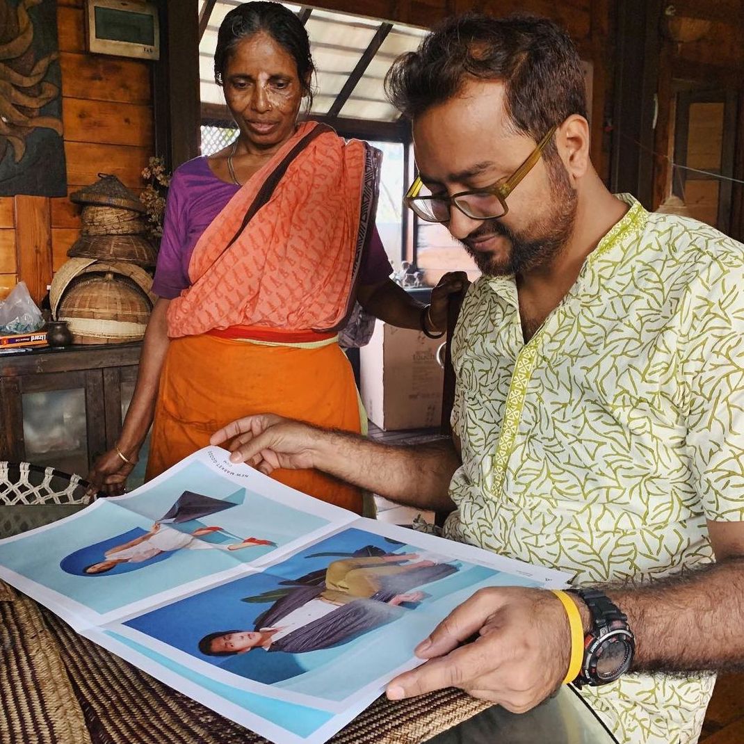 A seated man and a woman wearing a sari looking at fashion photographs in a newspaper catalogue.