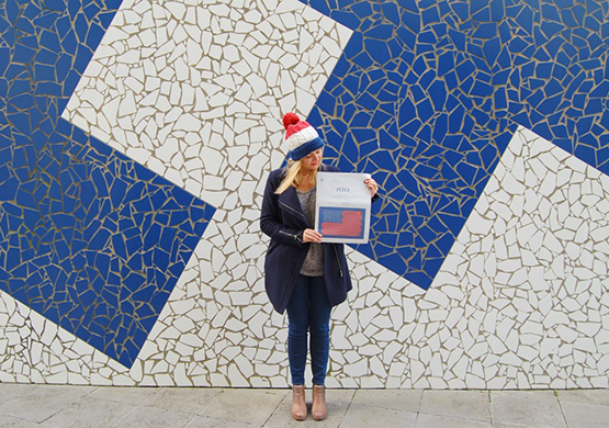 Woman stands holding a newspaper in front of a white and blue mosaic wall